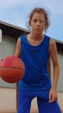 Vertical video. Teen boy playing basketball in playground at sunset in front of the camera