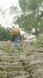 Vertical video. Success of the winner in the concept of adventure tourism. A woman with a backpack climbs up the ruins of the steps of an ancient amphitheater.
