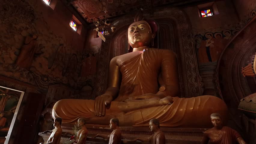 Huge Bronze Buddha Statue inside of the Buddhist temple with walls decorated with paintings and frescoes