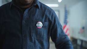 Anonymous African American male voter or businessman puts on badge with USA flag logo and inscription I Voted. US citizen at polling station during elections. National Election Day in United States. - Powered by Shutterstock - Get 15% off with code: PIKWIZARD15