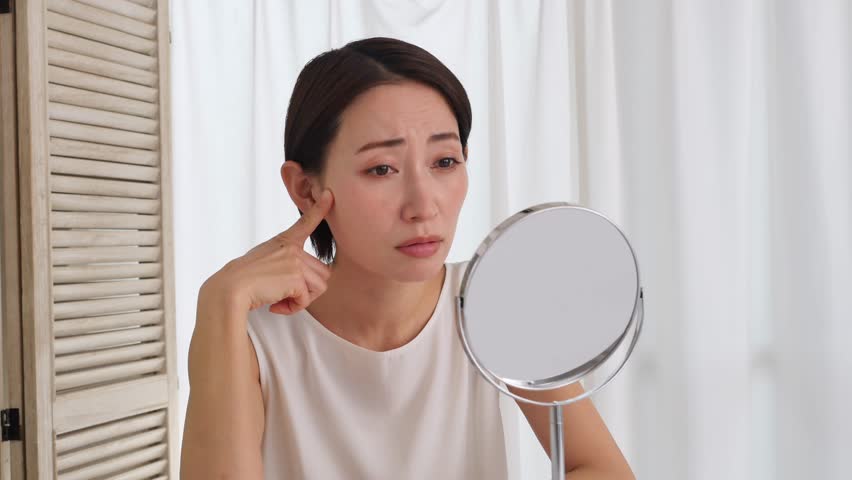 Asian middle aged woman looking in the mirror in the living room