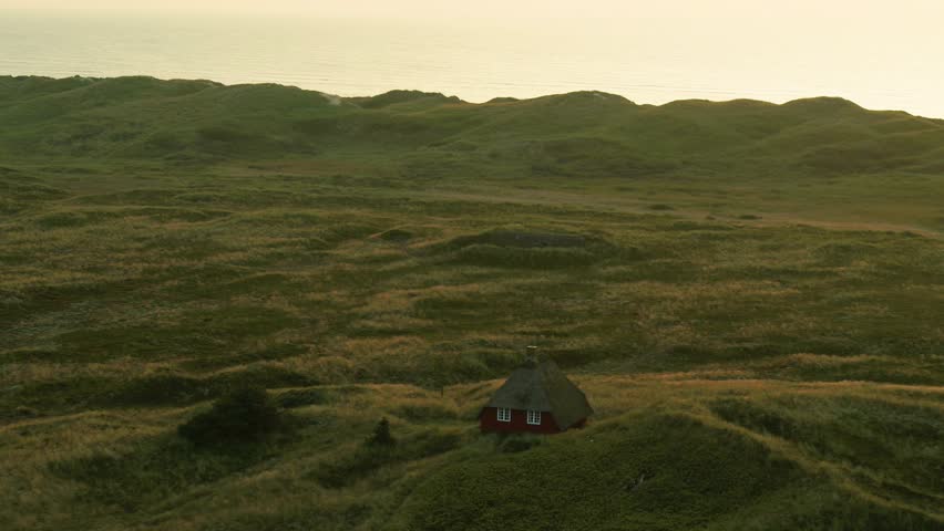 Drone pass beautiful old thatched roof summer house in the dunes in the marshland of Nymindegab in Jutland, on the Danish west coast. It is a beautiful sunny autumn day during sunset
