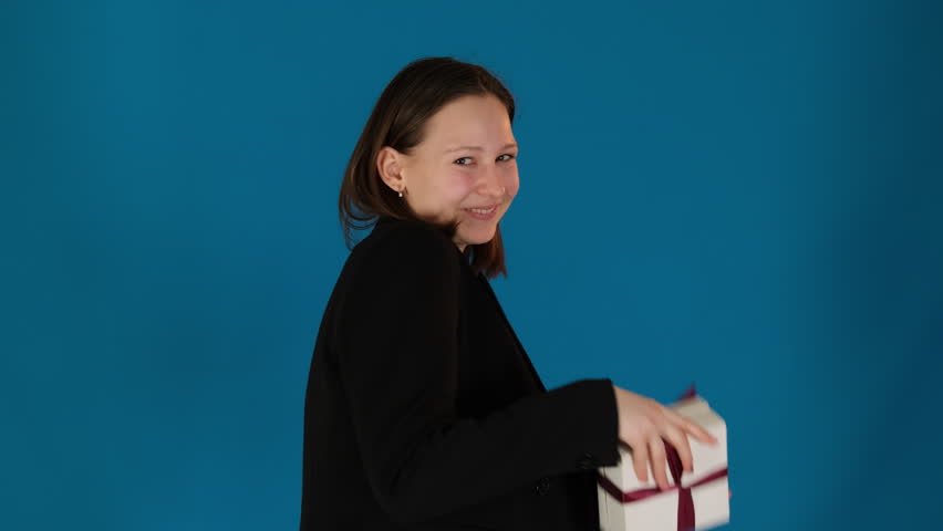 Lady eyes sparkle with anticipation presenting gift box. Happy young woman offers gift with outstretched arms on blue background