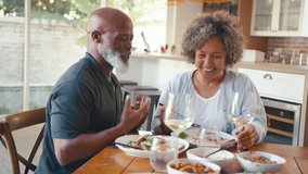 Smiling senior couple enjoying meal at home together doing cheers with glasses of wine sitting around table - shot in slow motion - Powered by Shutterstock - Get 15% off with code: PIKWIZARD15