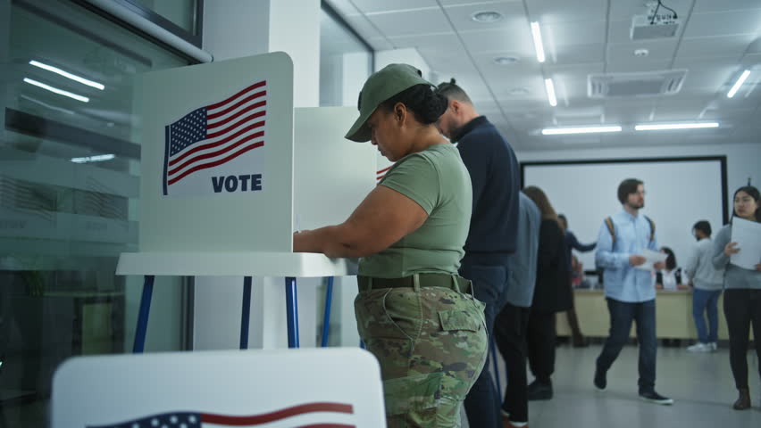 Female soldier and Asian woman vote in booths in polling station office. National Election Day in United States. Political races of US presidential candidates. Patriotism and civic duty. Dolly shot.