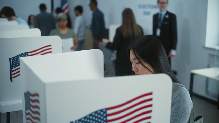 Asian female American citizen votes in booth in polling station office. National Elections Day in the United States. Political races of US presidential candidates. Civic duty and patriotism concept.