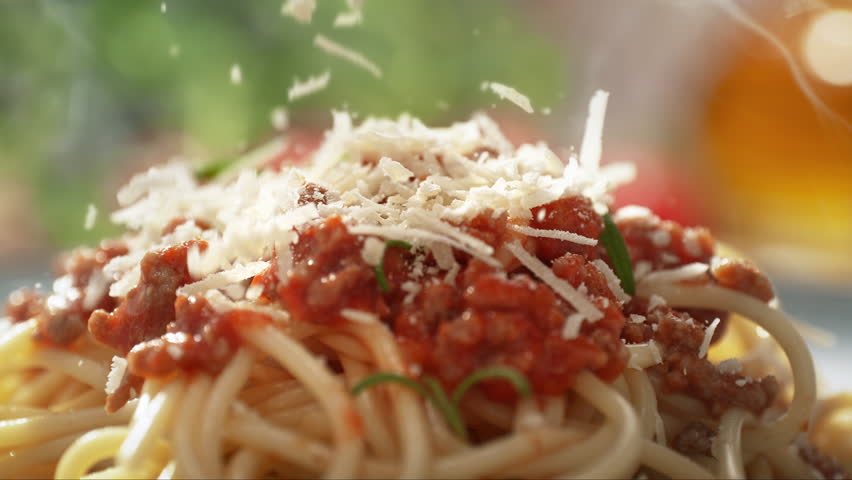 Sprinkling Grated Parmesan on Freshly Prepared, Served on a Plate, Spaghetti Bolognese with Tomato Sauce, Ground Beef and Rosemary