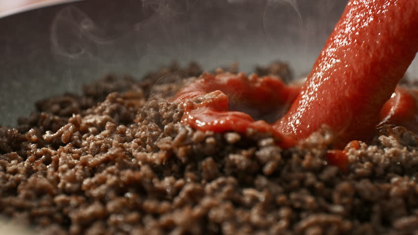 Ground Meat Frying in a Pan with a Stream of Red Tomato Sauce Pouring over it in Slow Motion - Cooking Spaghetti Bolognese in a Kitchen