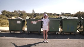 Shooting a straight video of a girl in a pink panama and light coloured clothes against a background of rubbish bins.  A girl smiling against a background of rubbish bins. Sorting the rubbish.