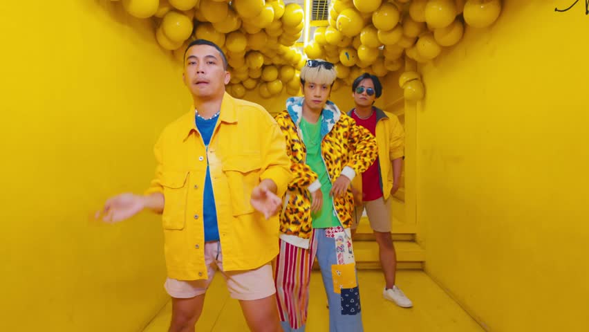 Three trendy young adults dancing in a vibrant yellow tunnel with dynamic poses and colorful outfits during the daylight