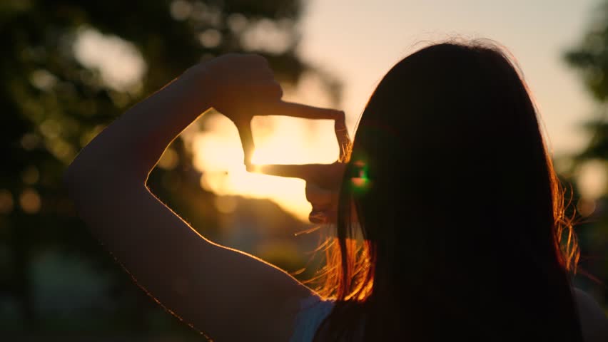 Seeing world as different Concept. Sees like in movies. Hands of a young female director cameraman making frame gesture at sunset. Business planning. Girl shows her fingers frame symbol in sun.