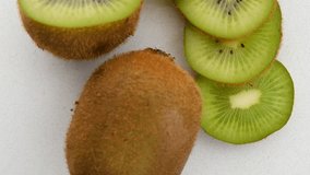 Close-up top view of whole and sliced kiwi rotating clockwise and on a marble surface