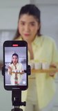Young female vlogger records a cooking tutorial in her kitchen, capturing the experience on her smartphone.