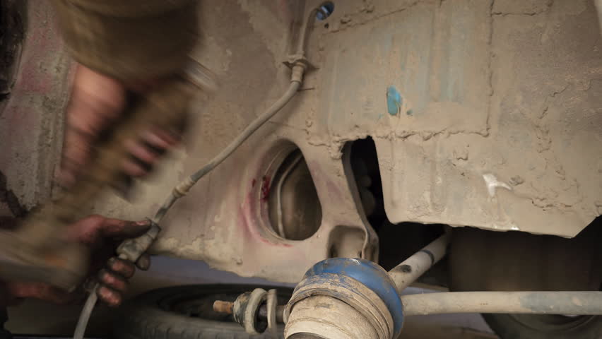 The calloused hands of hillbilly mechanic hitting driveshaft with a hammer during DIY car repairs. Closeup.