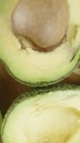 Vertical video. A multitude of avocado halves with pits are spread across the table, top view. I pick up one. Dolly slider, close up.