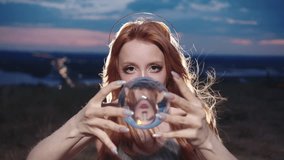 red-haired young woman, wearing a halo, is engaging in contact juggling with a see-through glass ball, against the backdrop of the evening sky. - Powered by Shutterstock - Get 15% off with code: PIKWIZARD15