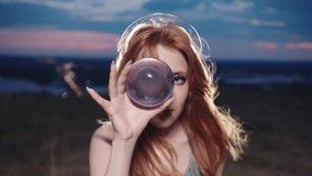Young red-haired woman stares at the camera through a transparent glass sphere. Her eye in the reflection seems to grow to a huge size thanks to the optical illusion. Medium shot. Slow motion. 4k - Powered by Shutterstock - Get 15% off with code: PIKWIZARD15