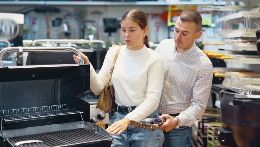 Couple of young man and young woman shoppers choosing BBQ grill in hardware store