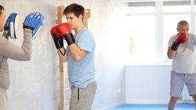 oncentrated sporty young guy in boxing gloves practicing self-defense techniques in gym, throwing punches on focus mitts in hands of instructor - Powered by Shutterstock - Get 15% off with code: PIKWIZARD15