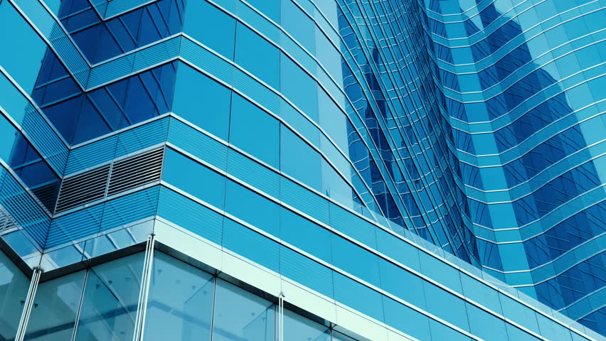 Abstract modern business architecture. Walls made of glass and steel with reflections of buildings and blue sky.
