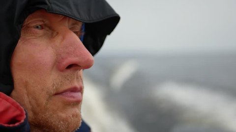 Close-up face of a man with a hood on his head. Fast speed floats on a boat on the sea, a strong wind is blowing and the boat is swinging on the waves. 3840x2160, 4k