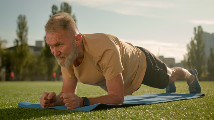 Caucasian old man in plank exercise workout training stadium city outside effort strain fitness athlete health muscular physical pose bodybuilder strong endurance power sporty determination practicing