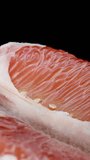 Vertical video. Close-up of the red veins of the pomelo flesh. Rotation on a black background.
