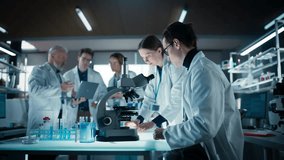 Head of Laboratory Making a Bioengineering Experiment with a Group of Young Science College Students. Future Specialists Working with Modern Microscopes, Using Tablet and Laptop Computers - Powered by Shutterstock - Get 15% off with code: PIKWIZARD15