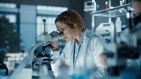 Cinematic Footage of a Female Bioengineer Looking at DNA Samples Under a Microscope in a Modern Applied Science Laboratory. Portrait of a Young Lab Engineer in White Coat Inventing New Medical Drugs - Powered by Shutterstock - Get 15% off with code: PIKWIZARD15
