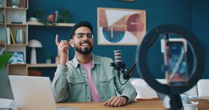 Vlogger working at recording room. Male blogger talking to listeners on stream. Podcasting or broadcasting. Recording sound. Man leading blog. Vlogger using laptop and microphone. Recording equipment.