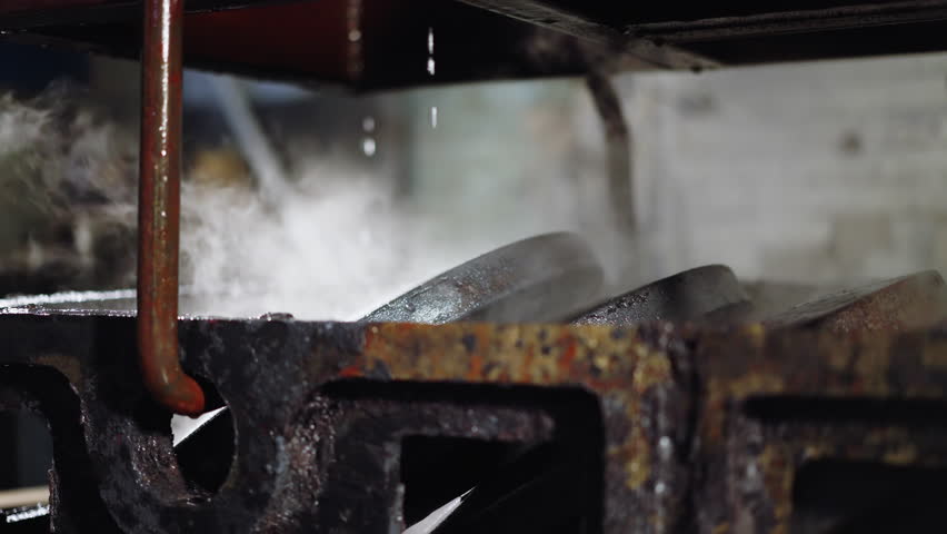 Steam rises from freshly quenched metal parts in a casting foundry's cooling station
