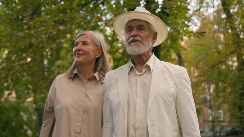 Happy Caucasian grandparents retired pair pensioners smiling woman man stroll together talk retirement outdoors city nature park. Joyful elderly couple female male talking enjoy walk outside parkland Royalty-Free Stock Footage #3480925359