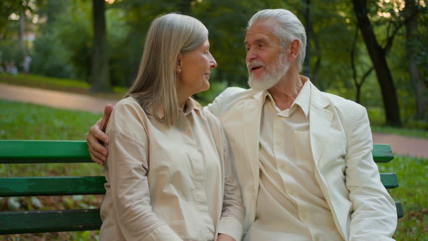 Relaxed cheerful Caucasian aged family grandmother woman grandfather man sitting park bench pair embracing planning retirement holidays spend weekend leisure outside green nature countryside parkland Royalty-Free Stock Footage #3480928111