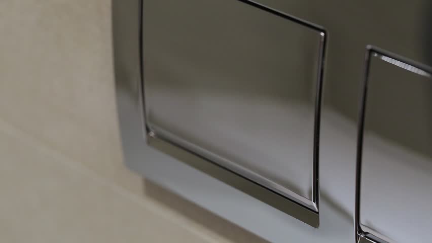 Woman pushing one button of two on wall at bathroom to flush toilet.