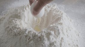 Close-up of female hands pouring chicken egg into wheat flour to knead dough on wooden table, satisfying video of ancient homemaking, charm of traditional homemaking techniques