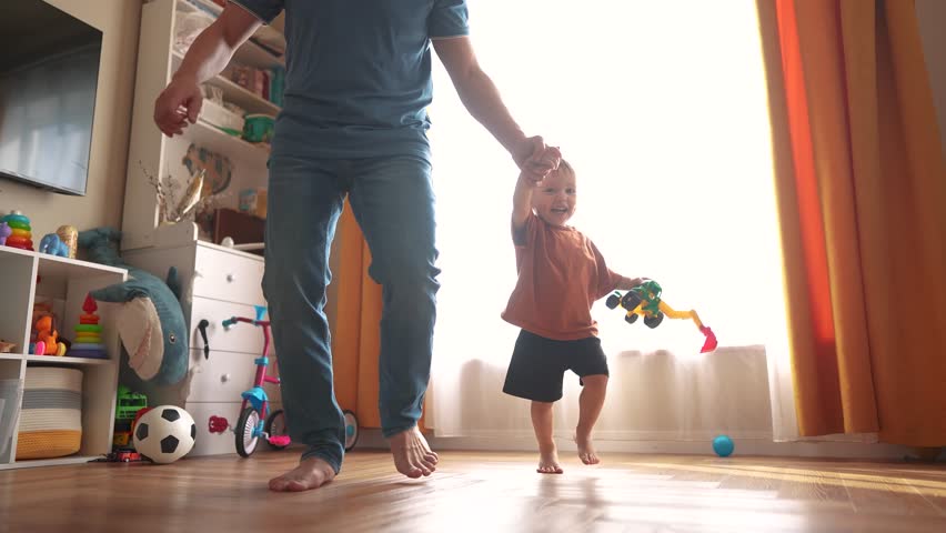 baby first steps with dad run. happy family kid dream concept. dad and baby son run along the corridor of the house indoors. dad and son care, hold hands, run, take first lifestyle steps
