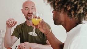 A gay couple shares a joyful breakfast moment, drinking orange juice and engaging in a lively conversation. - Powered by Shutterstock - Get 15% off with code: PIKWIZARD15