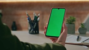 Unrecognizable employee watching chromakey smartphone education video sitting corporate workplace closeup. Woman hands holding mockup mobile phone at office. Girl looking green screen cellphone alone