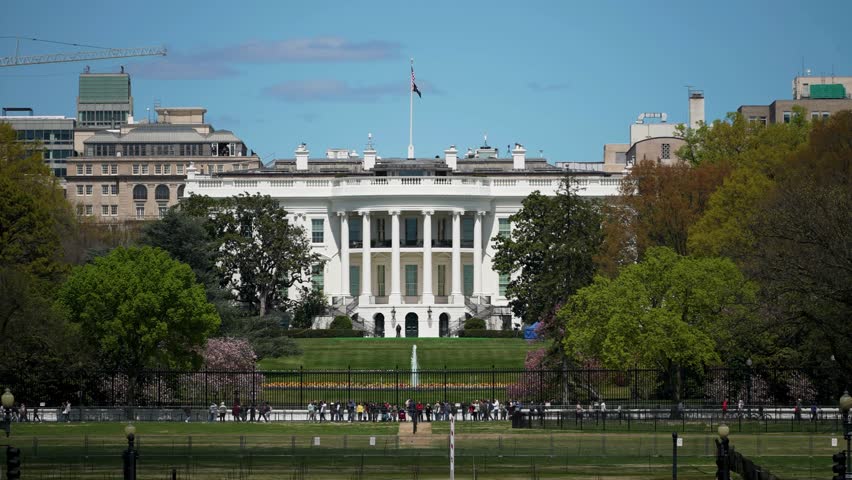 The oval office at the White House in Washington, DC, office of the president of the United States with tourists lined up at the gate on a bright summer day with clouds.