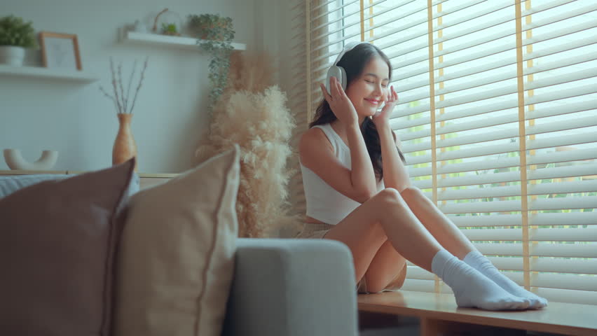 Happy carefree asian woman wearing headphones have fun moving listening to music relax in living room, Female enjoys listening chill music audio sound meditating feeling no stress at home in summer