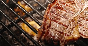 Close-up. Juicy covered with golden brown crust appetizing T-bone steak lies on grill grate, yellow flames fry steak, bringing taste to perfection, spreading appetizing aroma through air, copy space. 