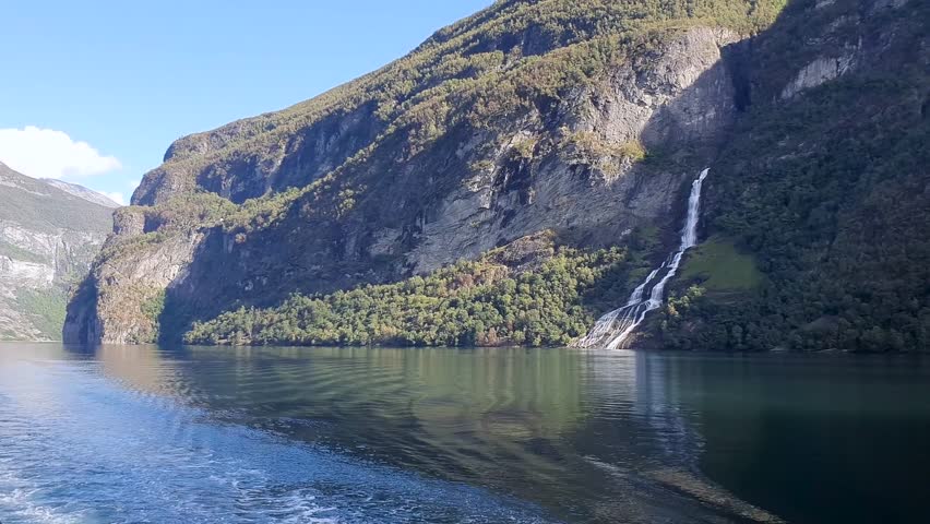 Stunning view of the beautiful Seven Sisters waterfall in the Geiranger fjord, Norway. Powerful streams of raging water fall from the 250m high jagged cliffs joining with the calm waters of the sea.