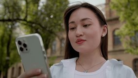 Young asian woman video call through smartphone at public park. Female in casual clothes talking on video call through mobile phone while relaxing in the park. 
