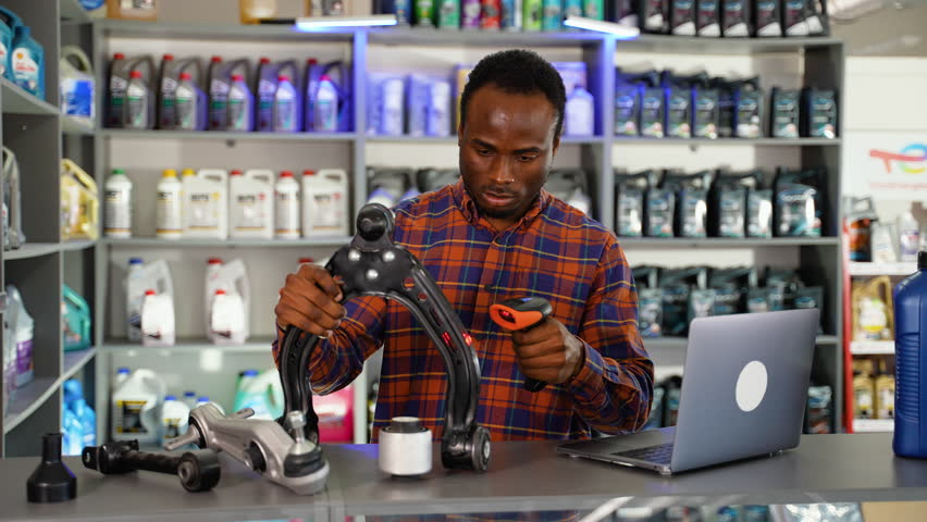 African american auto parts seller standing at counter making notes in laptop