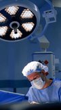 Surgeon working in modern surgery room. Round lamp illuminating the operational theatre. Vertical video.