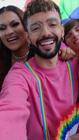 Vertical video of young group of LGBT people enjoying gay pride parade festival outside. Lesbian and gay friends having fun together celebrating LGBTQI festival event together in city street.