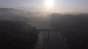 Foggy morning with mountains, rivers and forests in the background. Aerial footage of beautiful Indonesian view. Bridge crossing river in the morning. MOV video drone