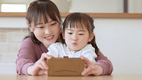 young asian mother and daughter using smartphone together in living room 
