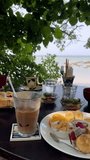 Vertical video of breakfast during holiday at the beach. Breakfast on the beach during summer holiday. Vertical filmed healthy summer food with fruit, ice coffee and a little salad. 