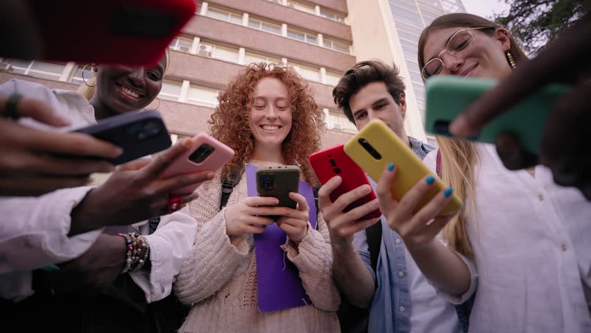 Low angle. Group of international young friends laughing gathered in circle using mobile phones. Cheerful people looking cells watching funny videos on networks. Addiction to technology of gen Z - Powered by Shutterstock - Get 15% off with code: PIKWIZARD15